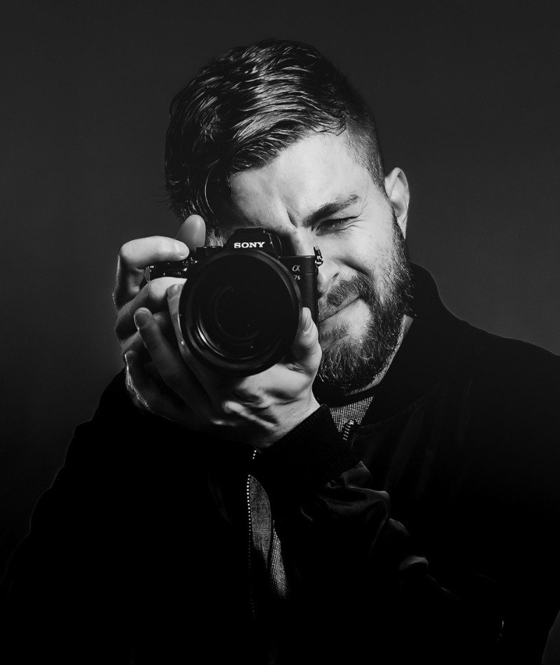 A black and white professional headshot of Mason Sterr, owner of Digital Fever Media, holding a Sony camera.